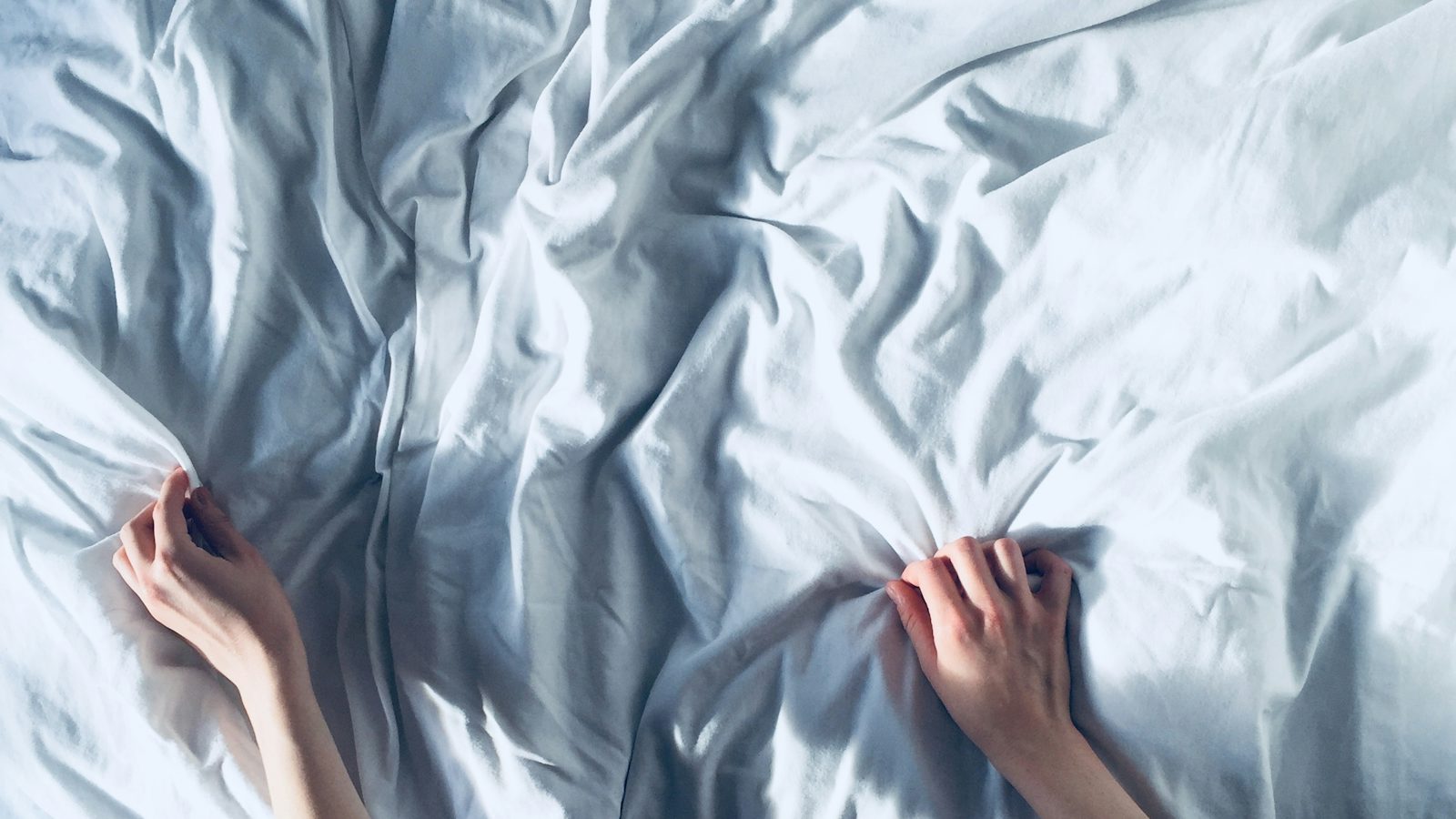 Mãos esticando um lençol branco sobre a cama