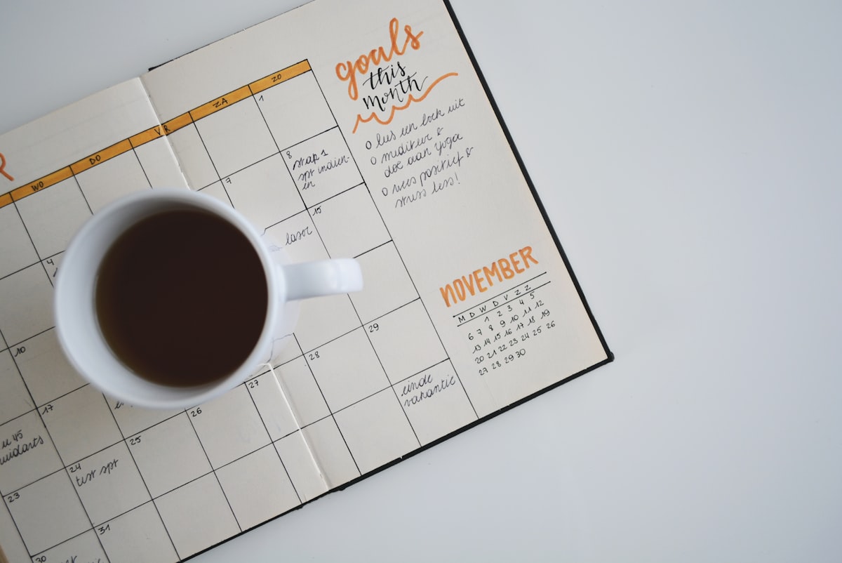 Xícara de café sobre uma agenda aberta em um calendário mensal, com anotações escritas à mão